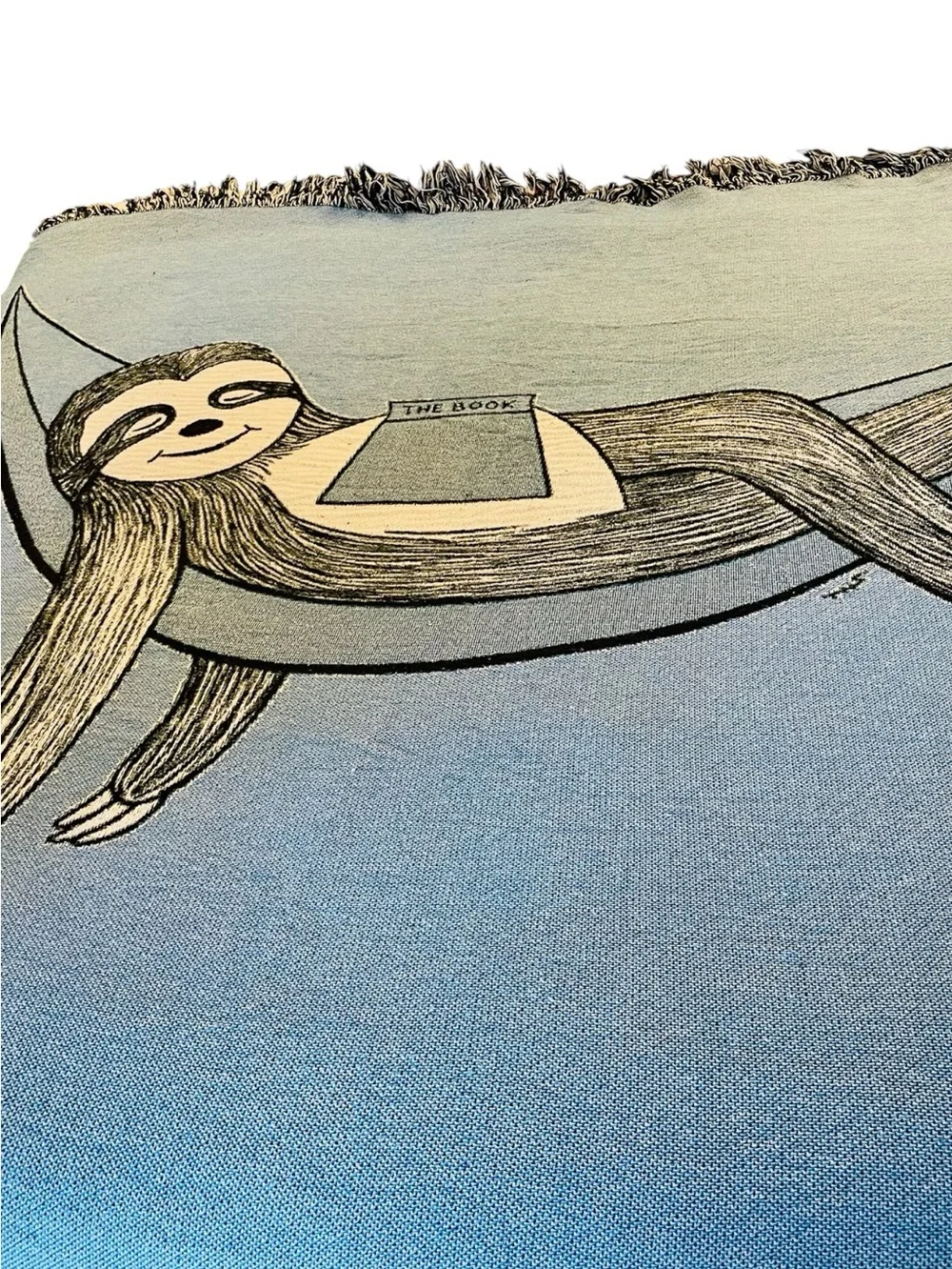 Outcasty cotton throw, relaxing sloth with book, shown on a Queen size bed